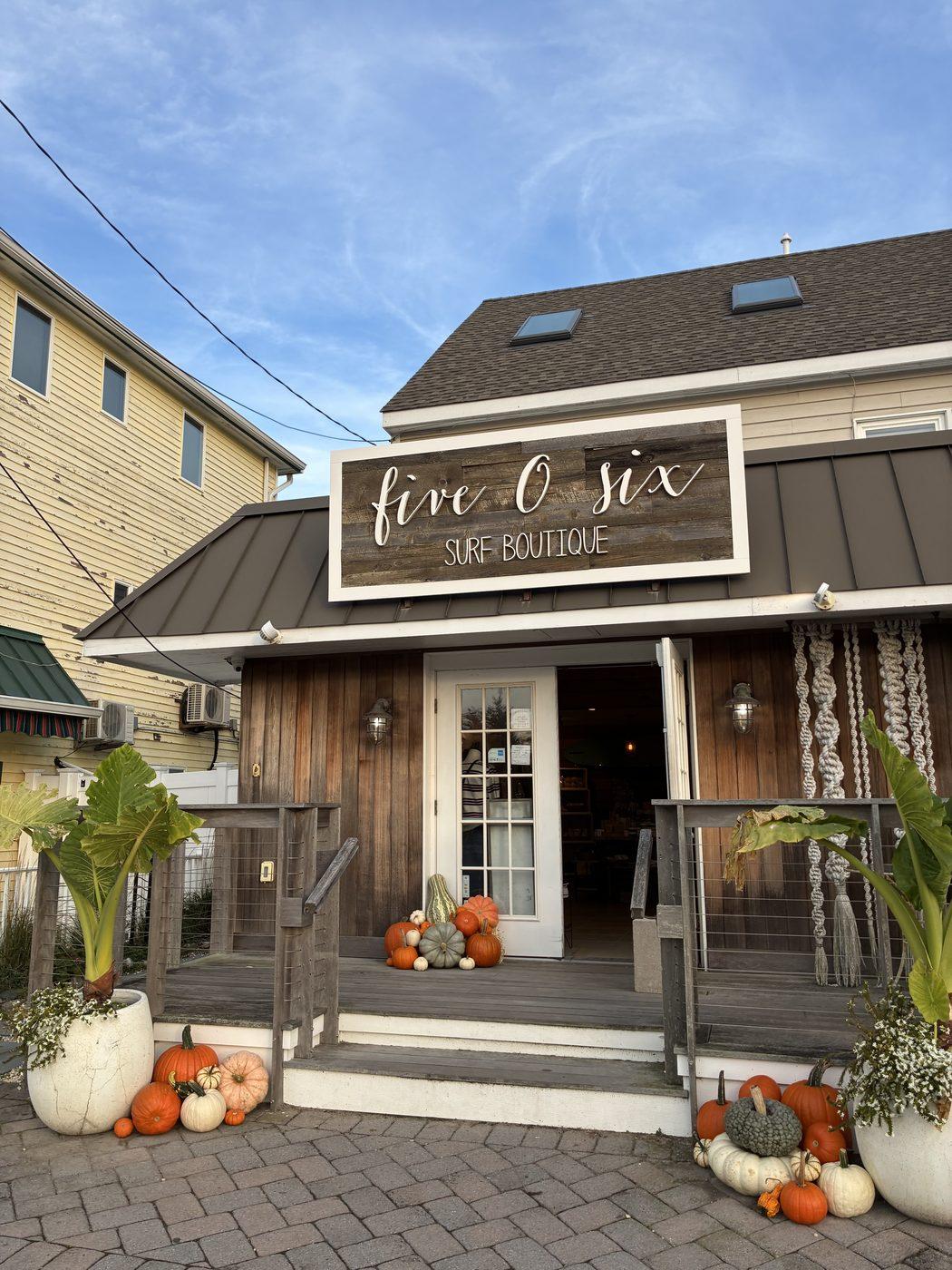 A weathered-cedar shopfront with pumpkins grouped on the steps and at both planters, in orange, cream and heirloom sage.